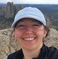 Heather Carmichael poses for photo on top of a rock in the mountains