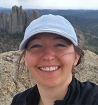 Heather Carmichael poses for photo on top of a rock in the mountains