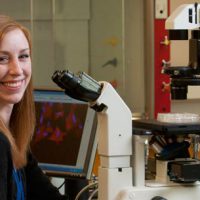 Kelly Widhammer sitting by high-tech microscope