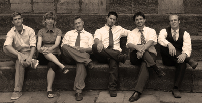 5 men and 1 woman sit cross-legged on a step - members of band Koine