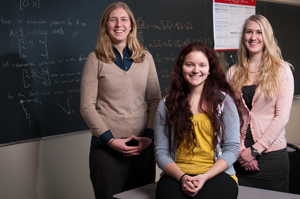 Three female students in front of a white board filled with mathematical equations