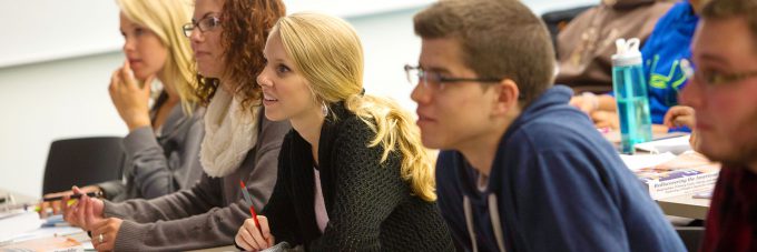 A line of students sitting in class, listening to speaker