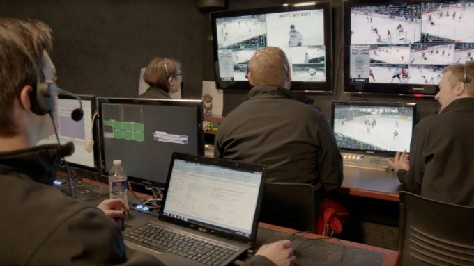 Students sit in front of tv screens and computer monitors while broadcasting the hockey game