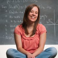 Mathematics student Tova Brown in front of a chalkboard displaying equations.