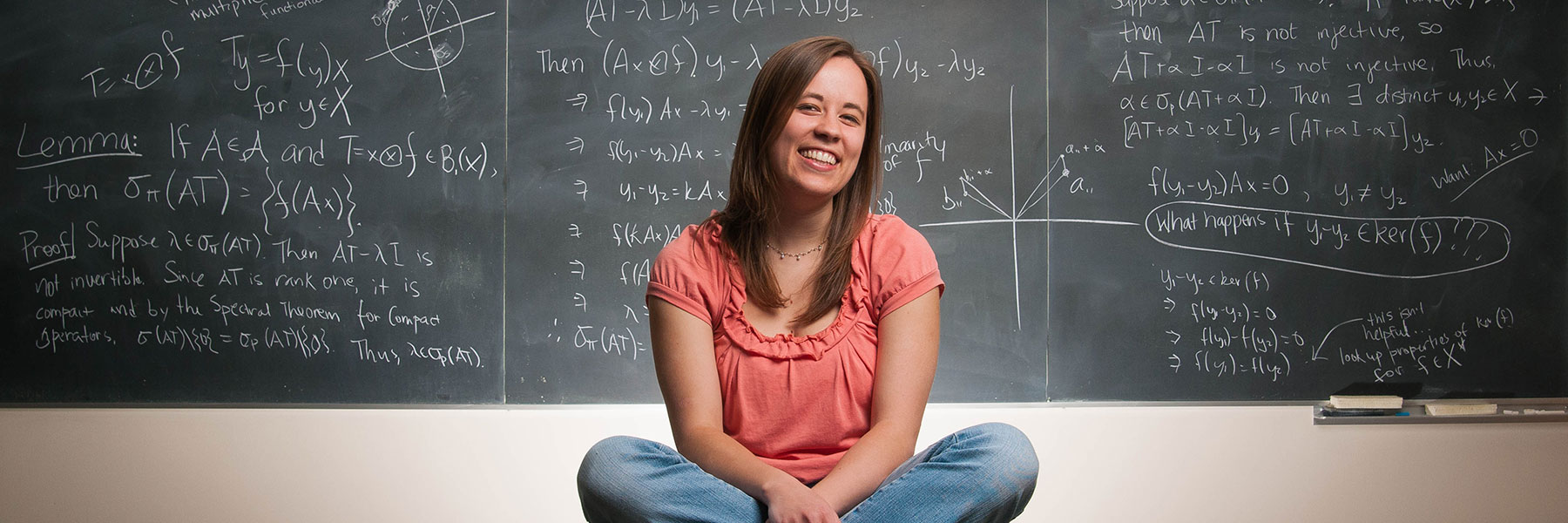 Mathematics student Tova Brown in front of a chalkboard displaying equations.