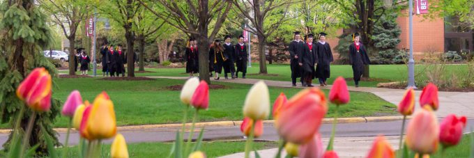 Graduates walking across campus before commencement