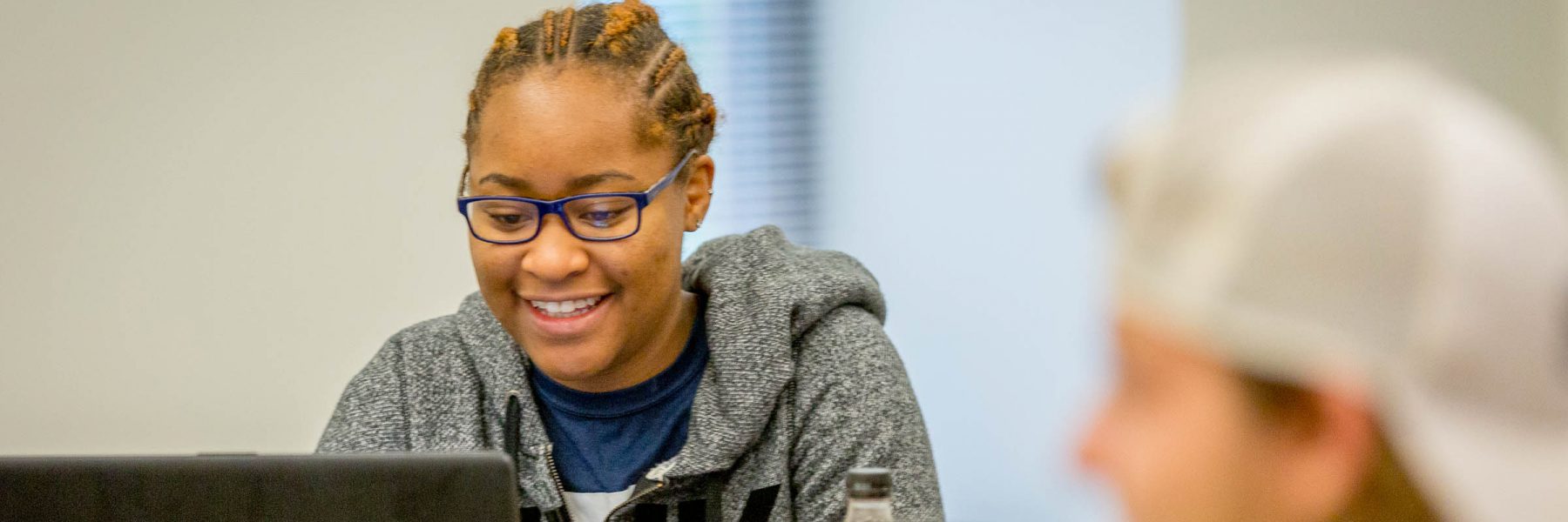 Female student smiling in class looking at laptop