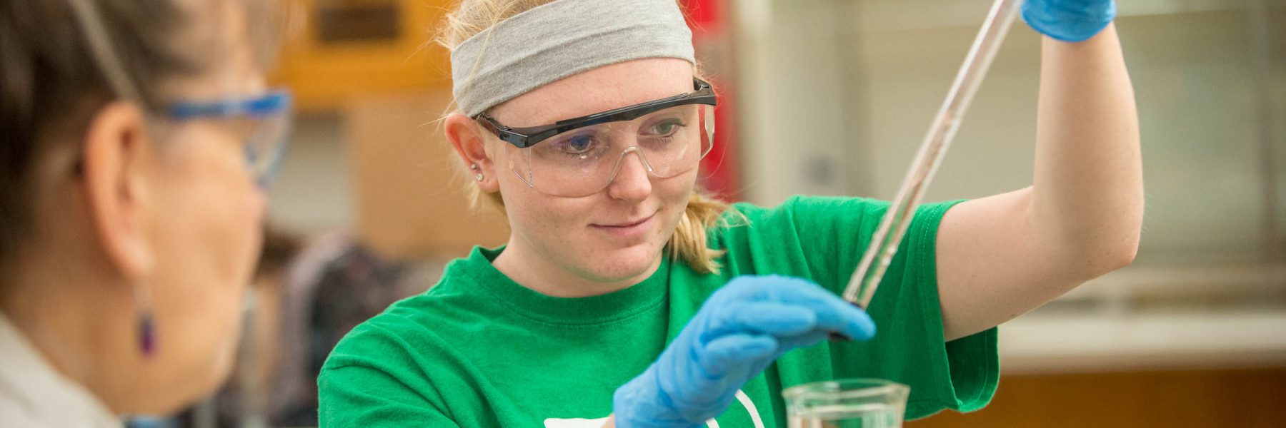 Student wearing protective equipment handles a test tube of liquid in class