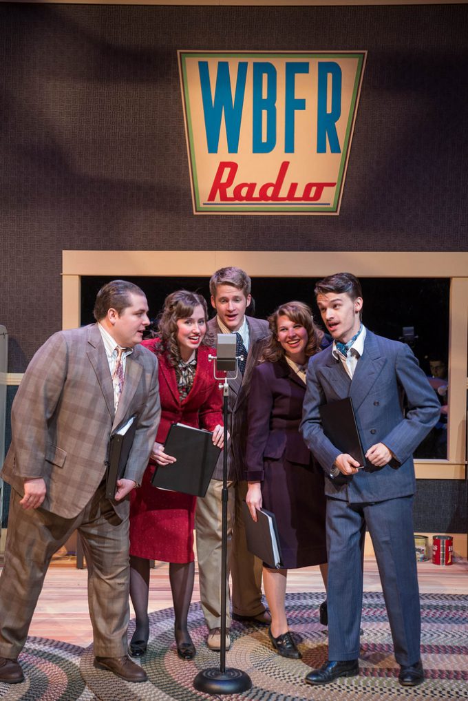 5 actors singing into old-fashioned microphone at a radio station (on stage)