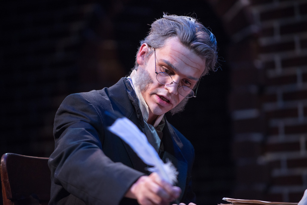 Actor portraying Ebenezer Scrooge dips the quill into the ink