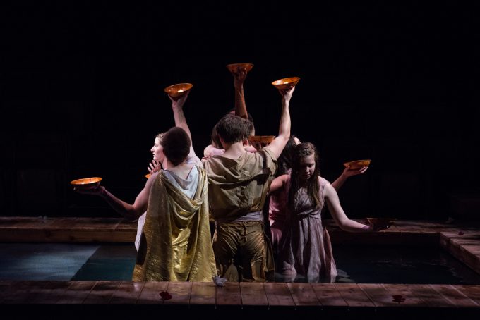 Actors standing in pool of water holding bowls of candles