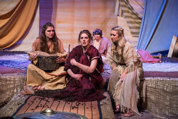 Four female actors in dresses sitting on stage