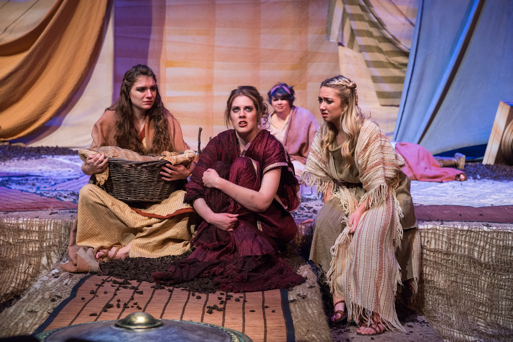 Four female actors in dresses sitting on stage