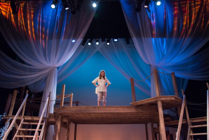 Female standing on platform on stage surrounded by sheer curtains