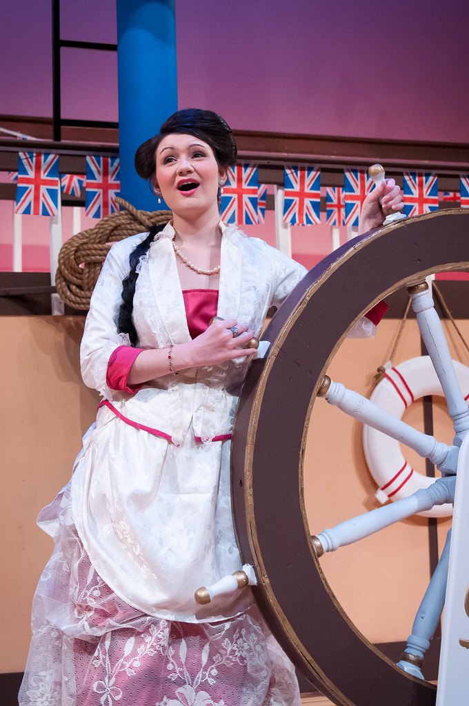 Woman holding on to wooden ship wheel and singing