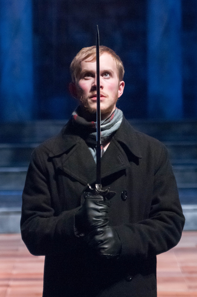 Man in black coat holding sword in front of his face