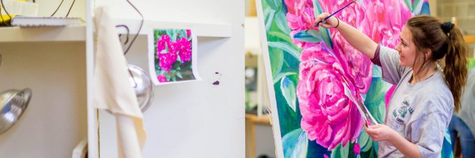 Female art student paints a green leaf on a large canvas of flowers in the art studio