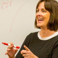 English professor smiles in front of whiteboard