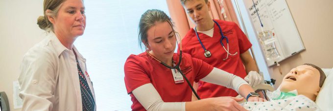 Professor assisting nursing student on correct placement of stethoscope on patient's chest