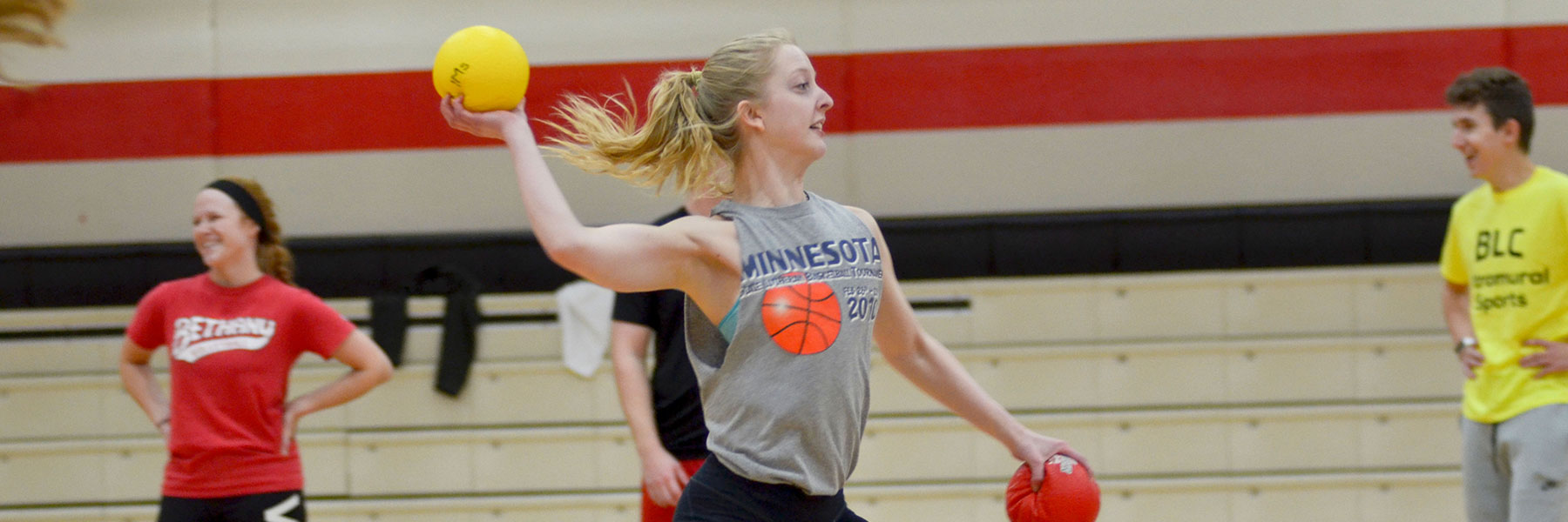 A student in the gymnasium throws balls during an intramural game as other students look on.