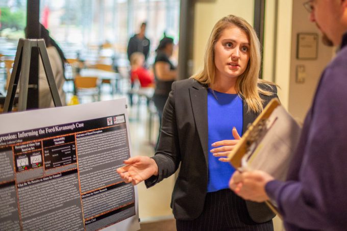 A student speaks with an attendee about her psychology research poster