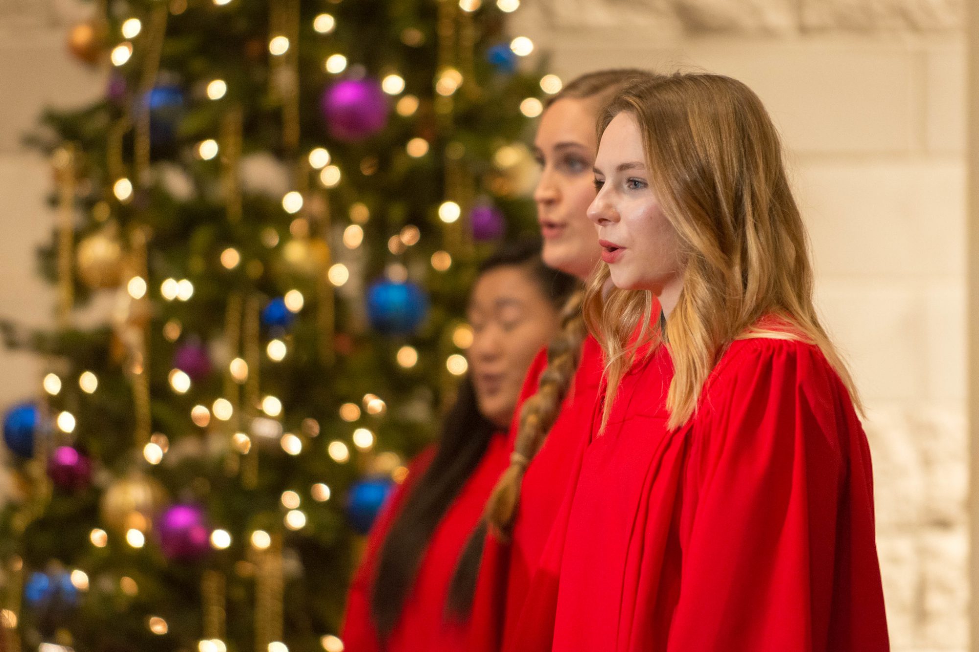 Closeup of three women of the choir singing at the Christmas at Bethany concert in December 2018, with a Christmas tree in the background