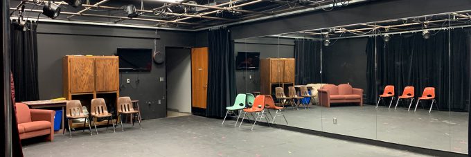 Black box theatre area - room with black floor, walls, curtains, one wall of mirrors, and chairs placed around the room