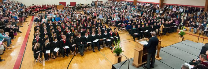 People seated in the Ronald J. Younge gymnasium for a commencement ceremony listening to the guest speaker at a podium.