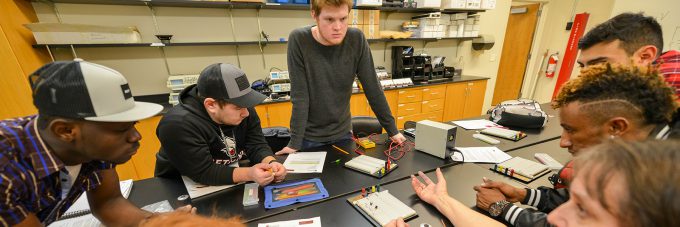 students gathered around table in electronics lab