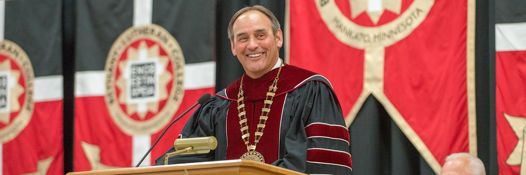 President Gene Pfeifer smiles at a podium during the 2019 commencement ceremony.