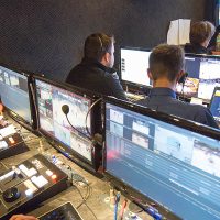 students work on computers and monitor activity on video screens during a tv broadcast