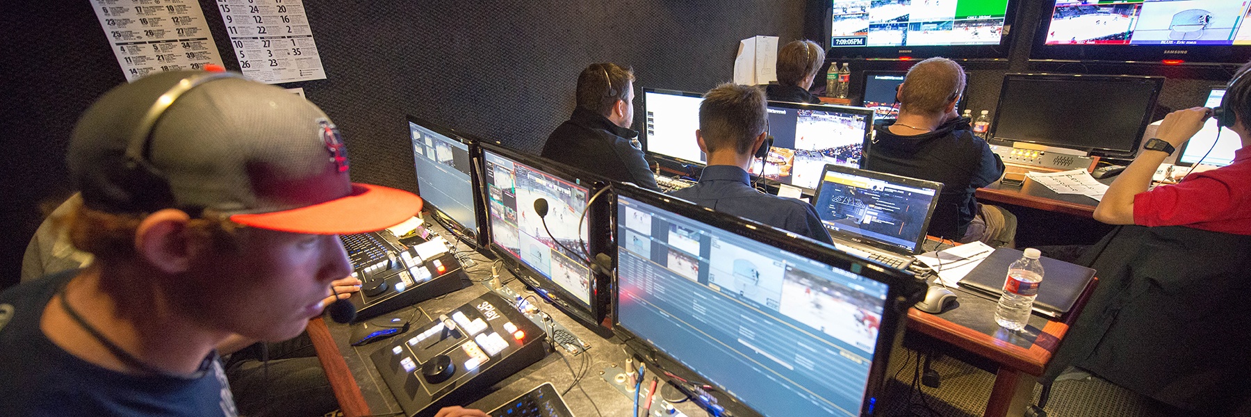 students work on computers and monitor activity on video screens during a tv broadcast