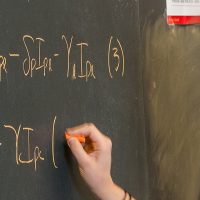 Student at chalk board writing out mathematic formulas.