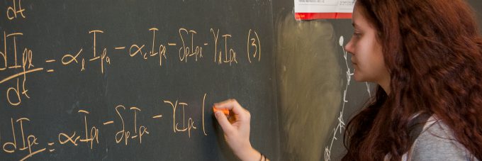 Student at chalk board writing out mathematic formulas.