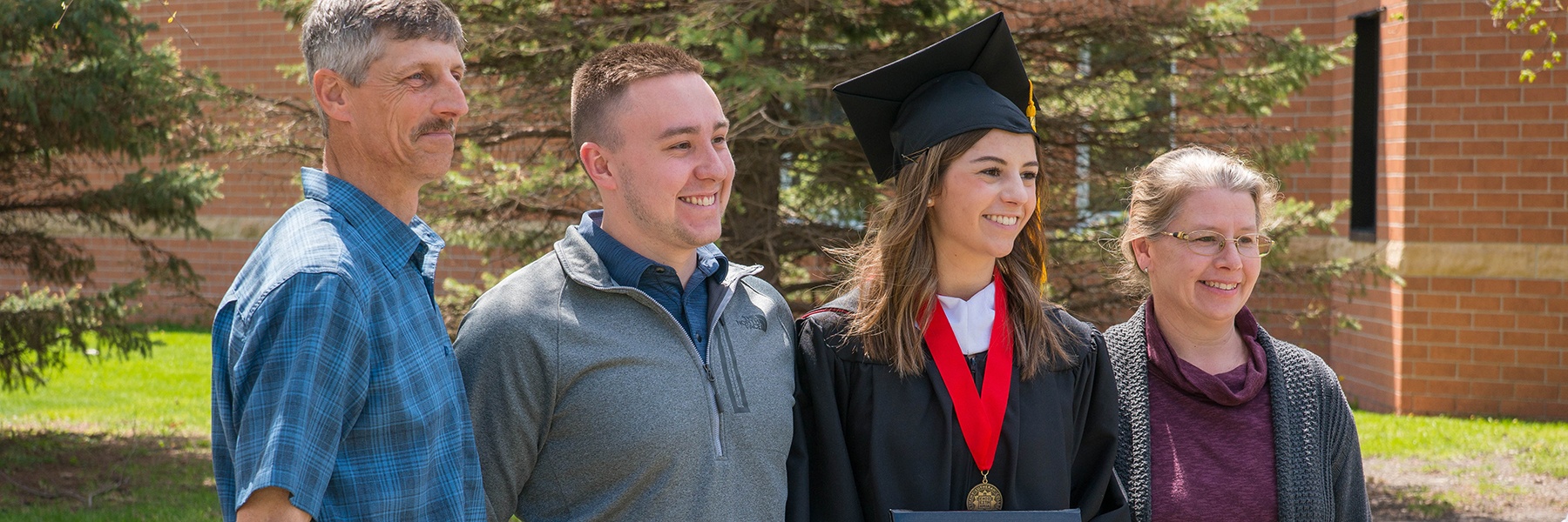 parents and a sibling pose with a graduate outside after commencement