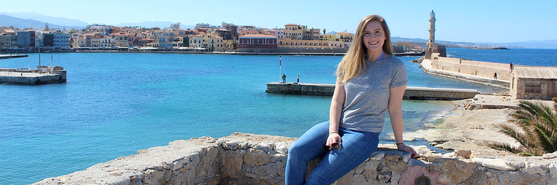 female student sitting on a wall in front of a body of water overseas