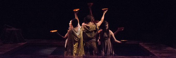 Theatre actors holding bowls with candles lighting up a dark room on stage