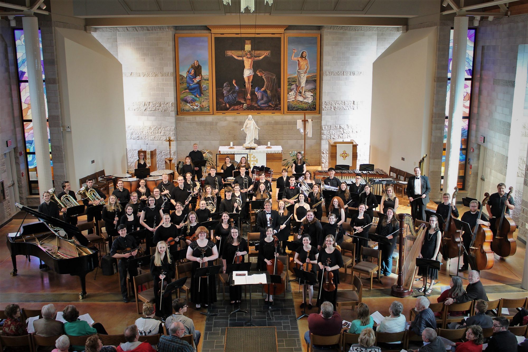 Concert Band and Chamber Orchestra standing with instruments in front of chapel