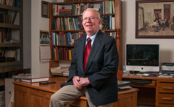 Dr. Peter Harstad sits on a desk in his home office.