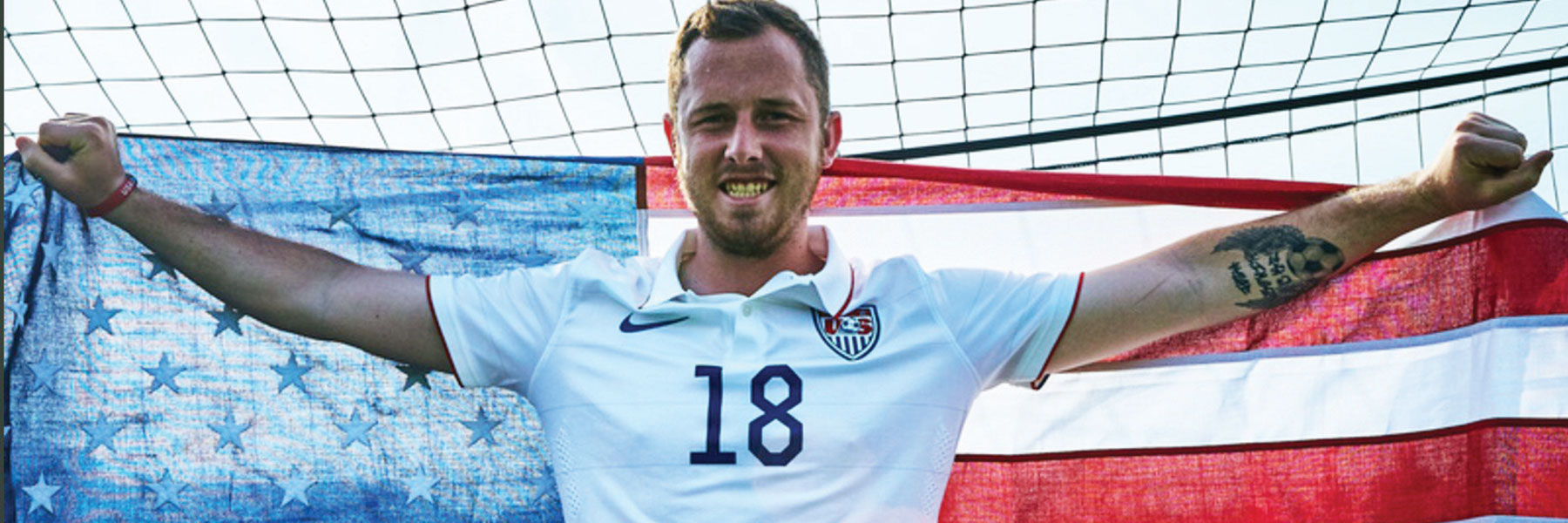 Wesley Shade poses with arms wide holding an american flag behind him