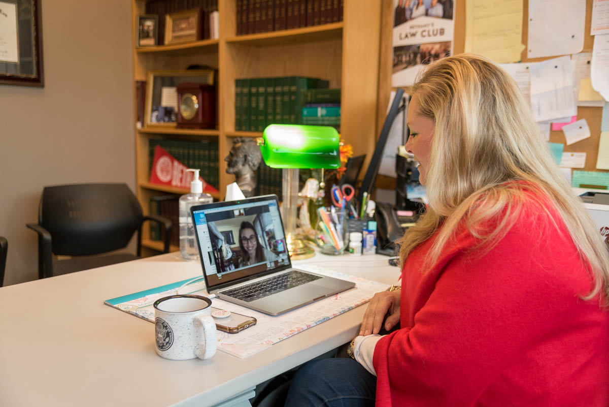 Associate Professor of Legal Studies Sara Edwards talks with a student remotely that is on shown on her laptop computer which is sitting on her desk