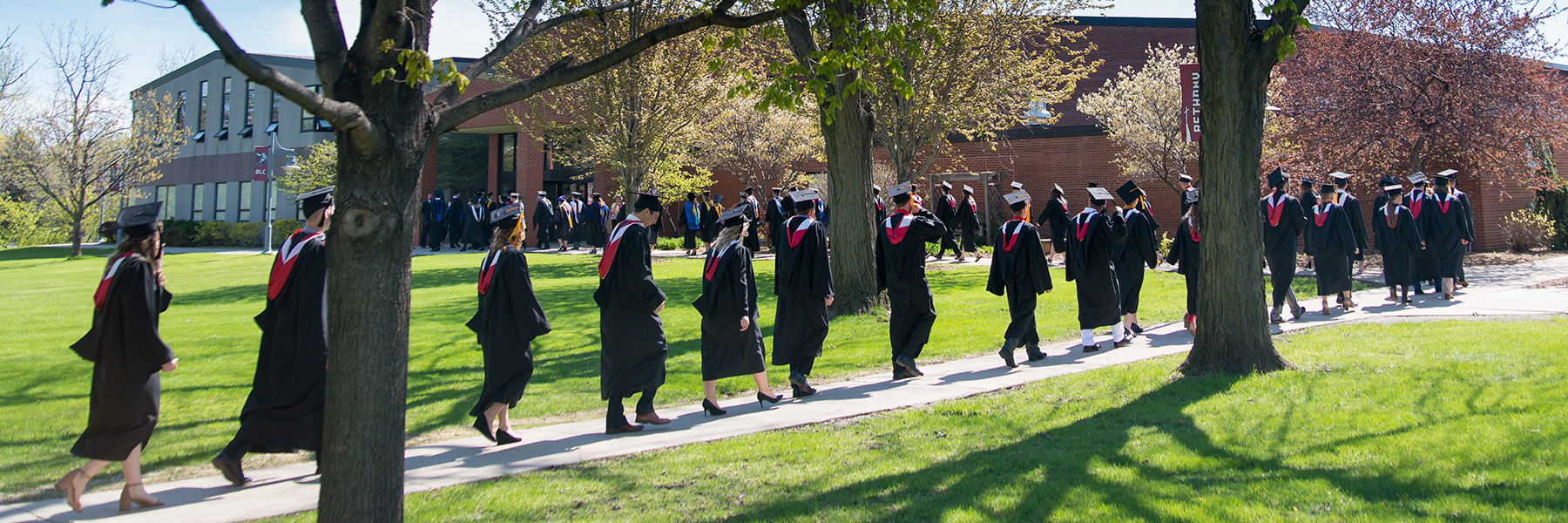 students walking on a sidewalk in graduation robes and caps