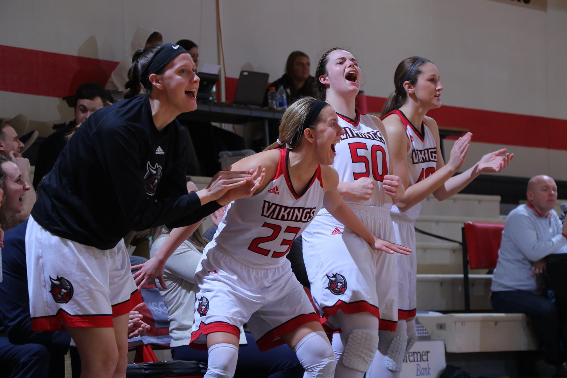 Four women's basketball players yell and cheer from bench