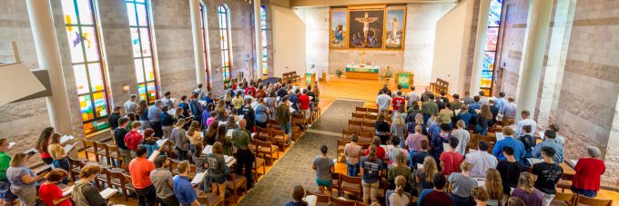 students, faculty, and staff standing in rows of chairs during a chapel service in trinity chapel