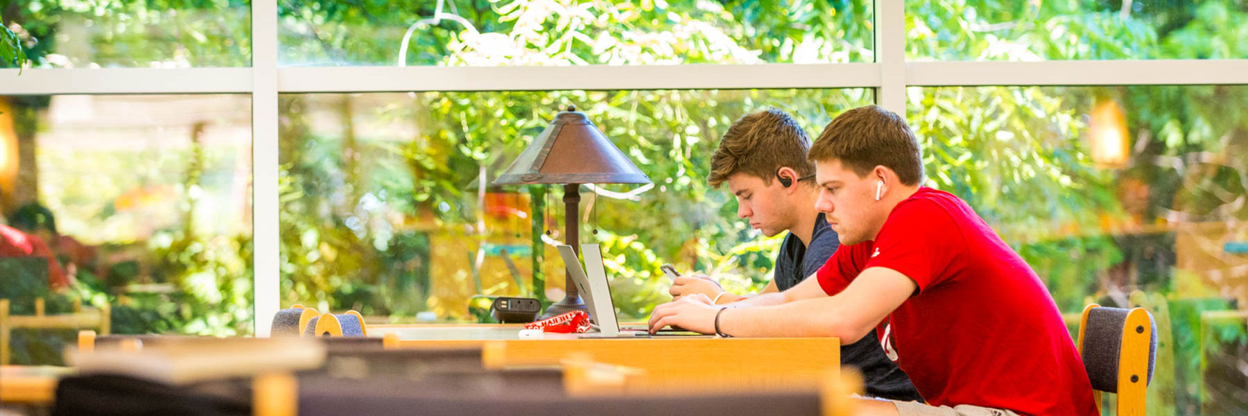 two male students seated at a desk look at their laptops while studying in memorial library