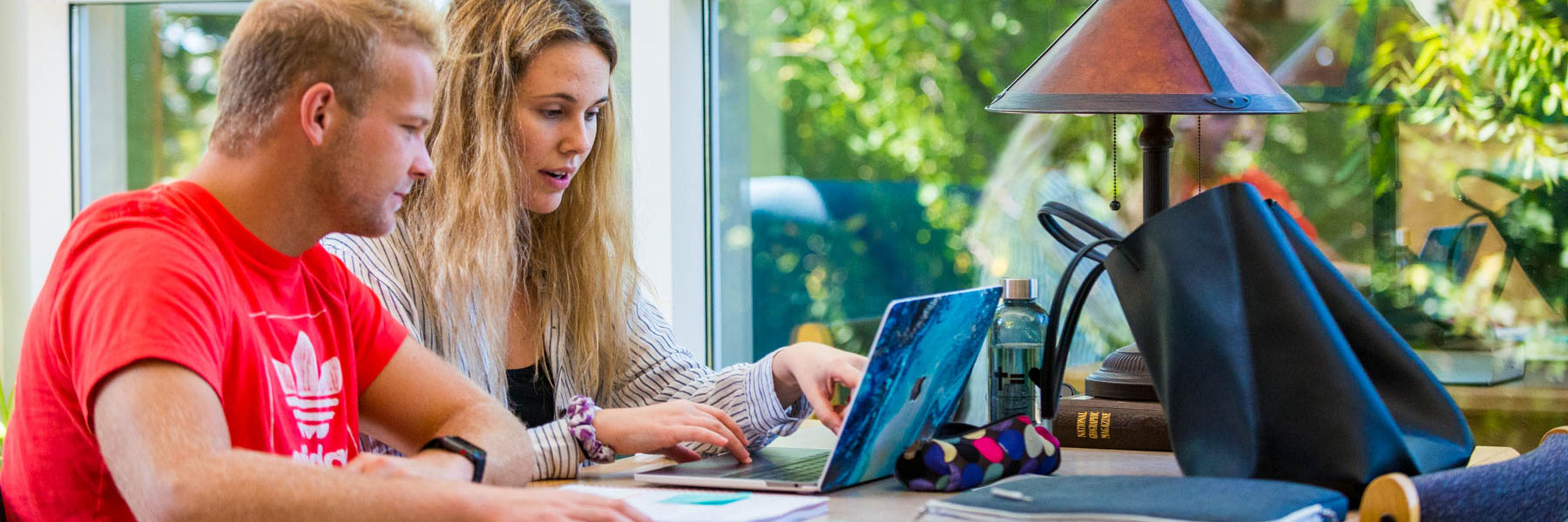 a male and female student look at a laptop on a desk while studying in memorial library