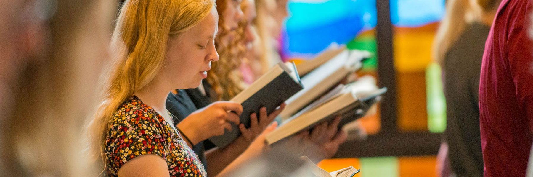 a female student is shown holding a hymnary while singing in a chapel service