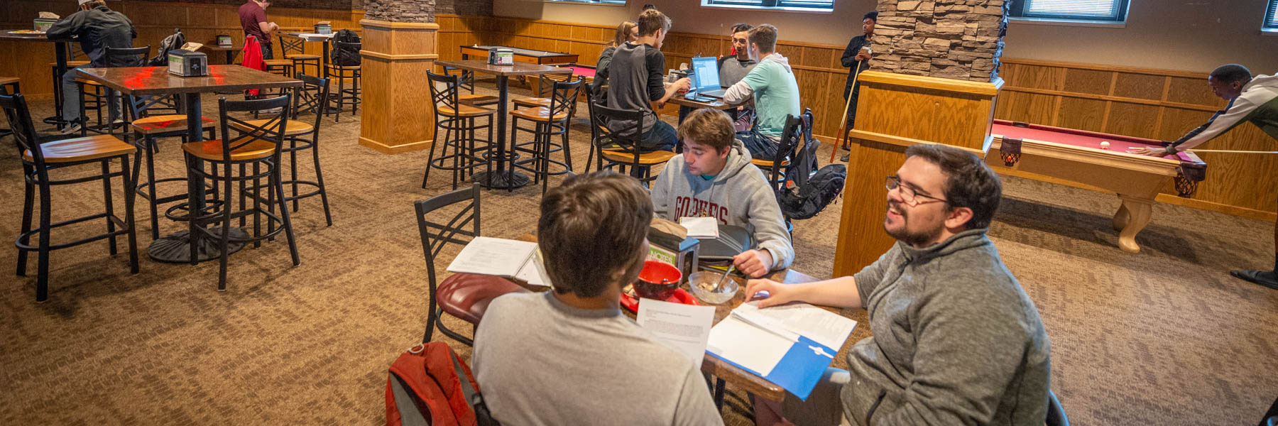 students are seated at table in the Viking Village while others are playing pool in the background