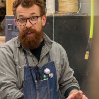 Professor Jaspersen talking to students while working in the sculpture studio