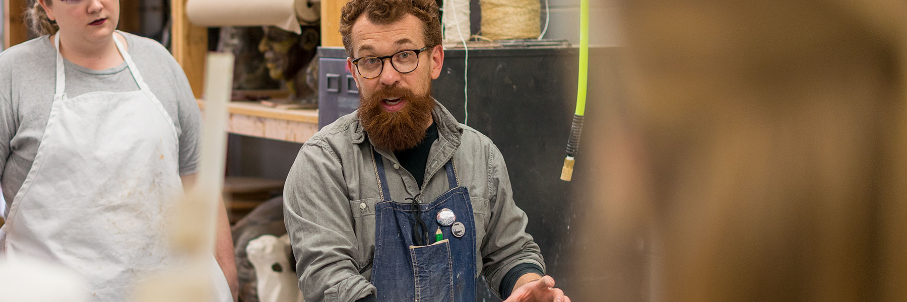 Professor Jaspersen talking to students while working in the sculpture studio